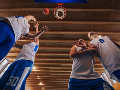 From a low angle, kids are seen actively playing basketball under the hoop, capturing the energy and movement of the sport